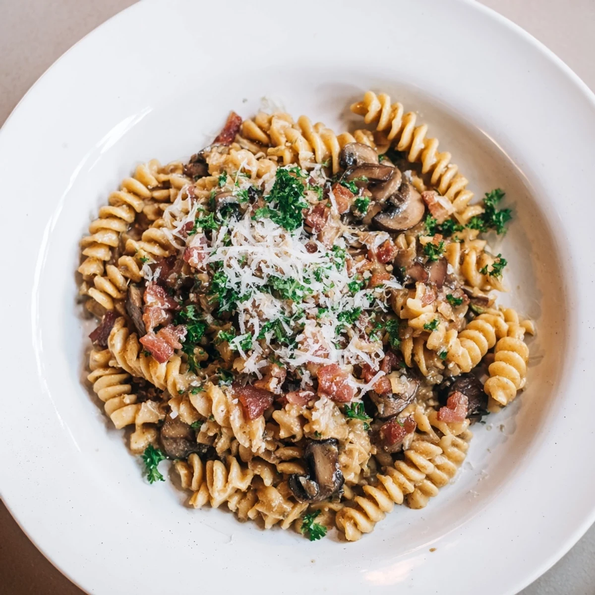 Steaming bowl of fusilli with bacon, onions, and mushrooms, a comforting pasta dinner.