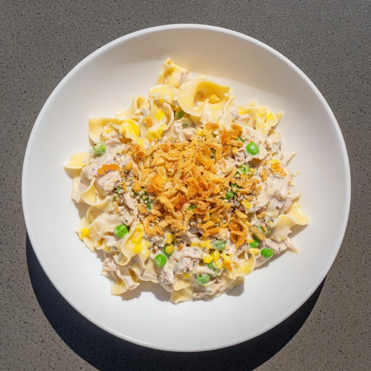 A close-up of a warm, creamy tuna noodle casserole topped with crunchy fried onions, ready to eat.