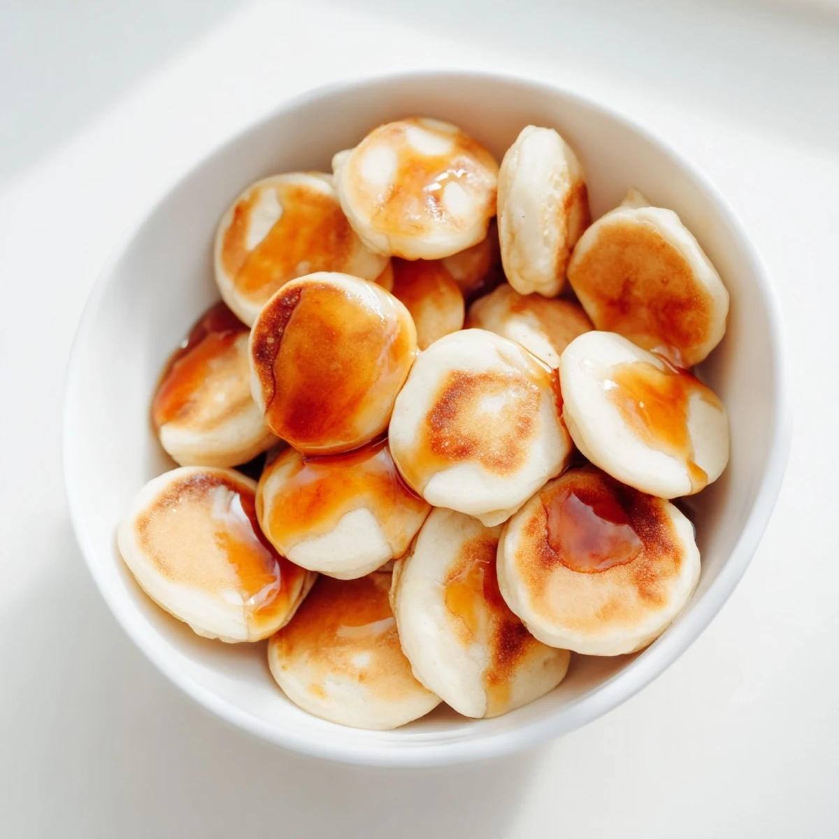 A bowl overflowing with golden Fluffy Pancake Cereal, drizzled in maple syrup and ready to eat.