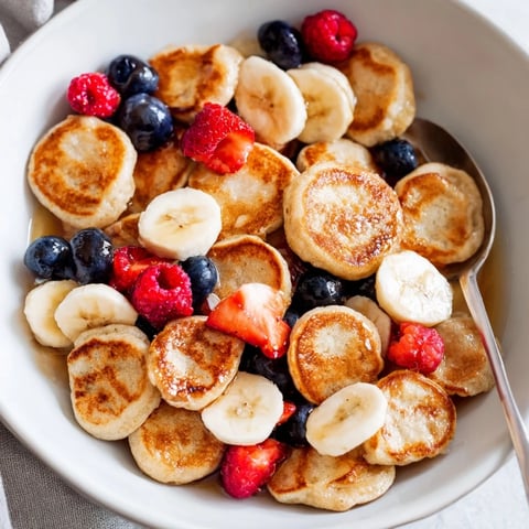 Adorable mini pancake cereal served in a bowl with fresh berries and syrup.  