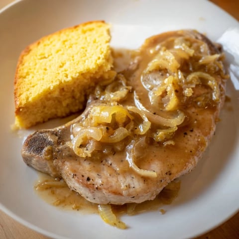Golden-brown smothered pork chops swimming in savory gravy, with warm and fluffy cornbread alongside.