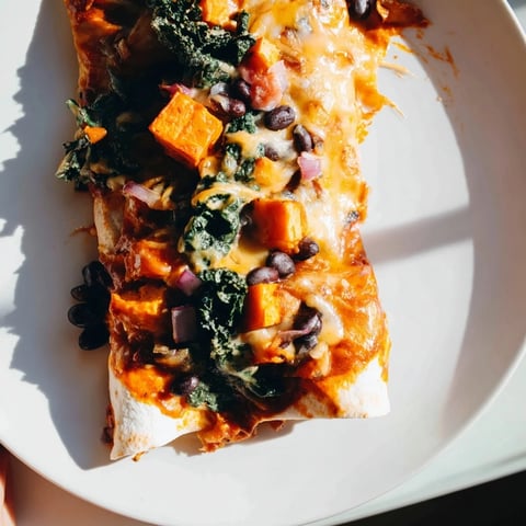Roasted sweet potato, black bean & kale enchiladas baking with bubbly cheese and savory enchilada sauce.