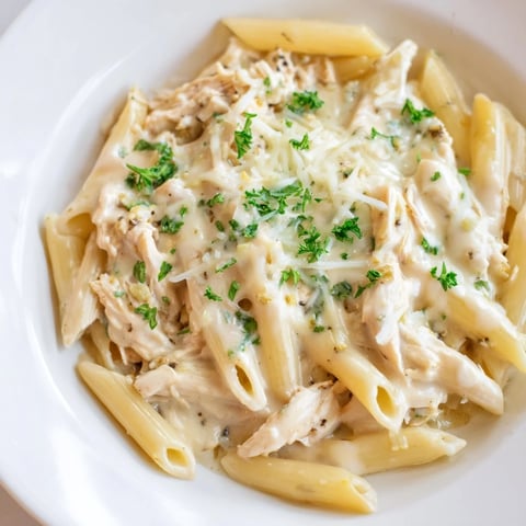 Image of Tinis Creamy Chicken Pasta, a warm bowl with Parmesan and parsley garnish.