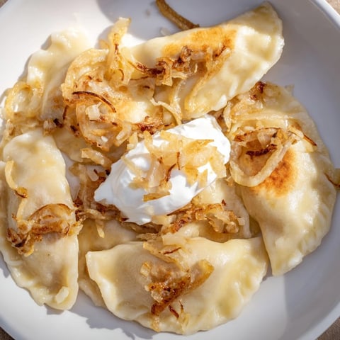 Golden-brown Polish pierogi dumplings are served with sweet caramelized onions and sour cream.