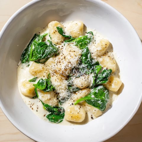 Creamy Garlic Gnocchi in a rich white sauce with wilted spinach served on a rustic plate.