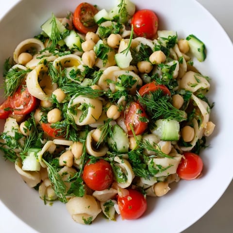 Freshly cooked chickpea pasta tossed with crisp cucumber, cherry tomatoes, and a zesty lemon herb dressing in a serving bowl.