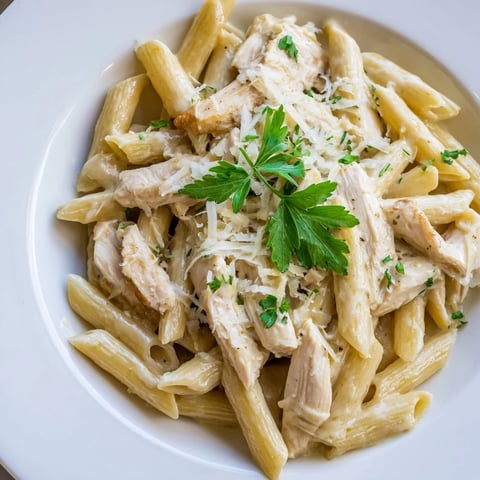 Golden roasted garlic cream sauce clings to al dente penne and tender, juicy chicken slices, garnished with fresh parsley.