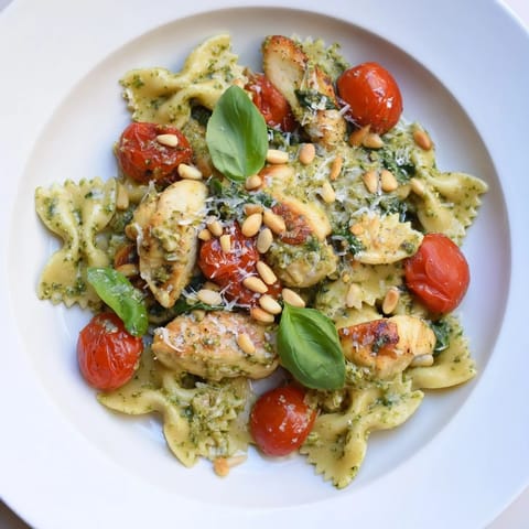 Close-up of creamy pesto chicken bowtie pasta, garnished with fresh basil and toasted pine nuts.