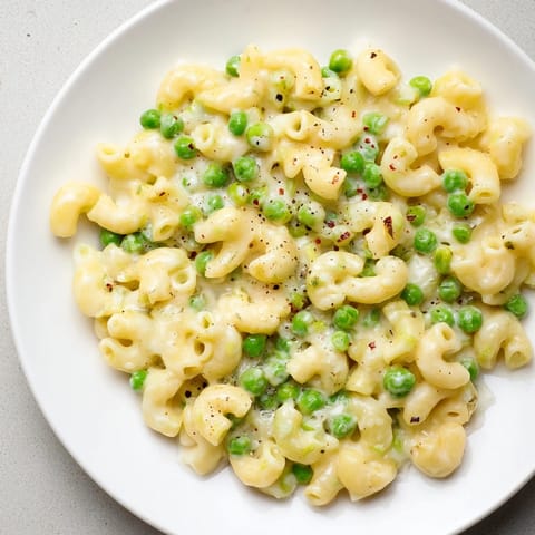 A close-up of buttery Macaroni & Peas, garnished with fresh herbs and Parmesan cheese.