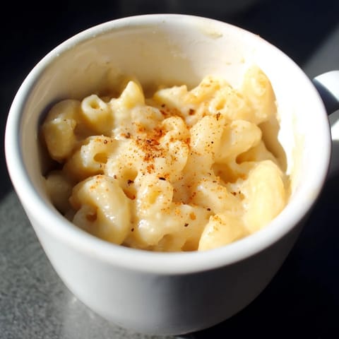 A close-up of creamy, homemade mug Mac & Cheese, sprinkled with Parmesan and paprika.