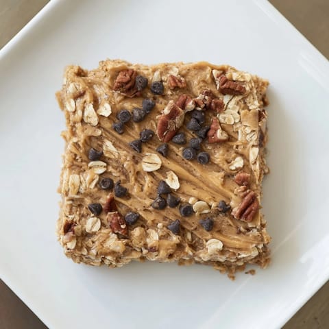 A close-up of a Peanut Butter Banana Oat Bar, ready to eat, with oats and chocolate chips.