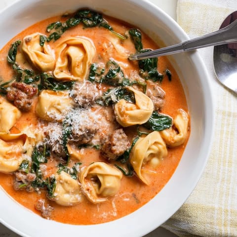 Hearty Tuscan Tortellini Soup ladled into a white bowl, garnished with Parmesan and fresh basil.