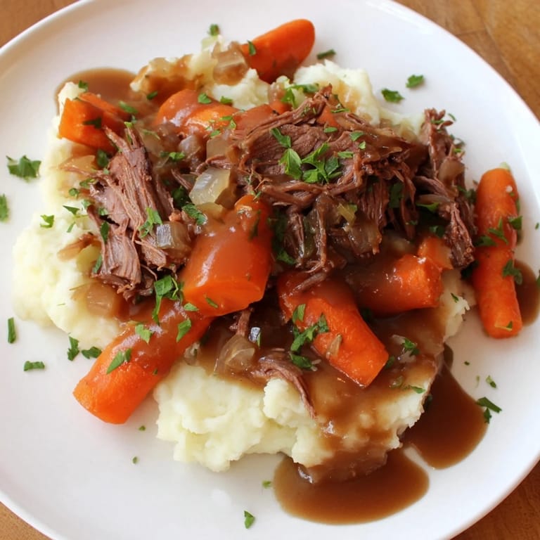 This close-up shows a delicious plate of slow cooker pot roast, surrounded by creamy mashed potatoes.