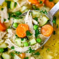 Hearty Spring Garden Chicken Soup in a rustic bowl, garnished with fresh parsley, lemon slices, and vibrant peas and carrots.