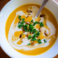 Silky smooth Butternut Squash Soup in a rustic white bowl, garnished with toasted pumpkin seeds and fresh parsley.