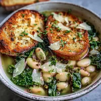 Hearty Tuscan white bean soup with kale and lemon zest in a rustic bowl, topped with Parmesan and olive oil.